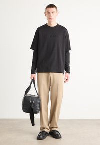 Black short-sleeve t-shirt with Calvin Klein logo, beige trousers, black bag, and chunky black shoes. Smooth textures and relaxed fit.