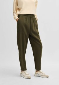 Olijfgroene, lichtgewicht tapered broek met een elastische tailleband, zijzakken en gestikte details. Gecombineerd met beige sneakers.