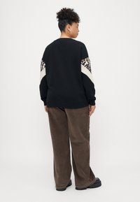 Juoda sportinė palaidinė su leopardų raštu ant rankovių, kreminiai akcentai, derinama su rudomis šviesaus velveto kelnėmis ir masyviais juodais batais.