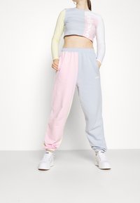 Lehce texturovaný pastelový dvoubarevný krátký top v modré a žluté barvě s logem; odpovídající modré a růžové tepláky s kapsami a elastickými lemy.