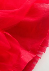 Rode tule stof met een zachte, doorzichtige textuur, voorzien van gestikte randen en gelaagde rimpels aan de onderkant voor extra detail.