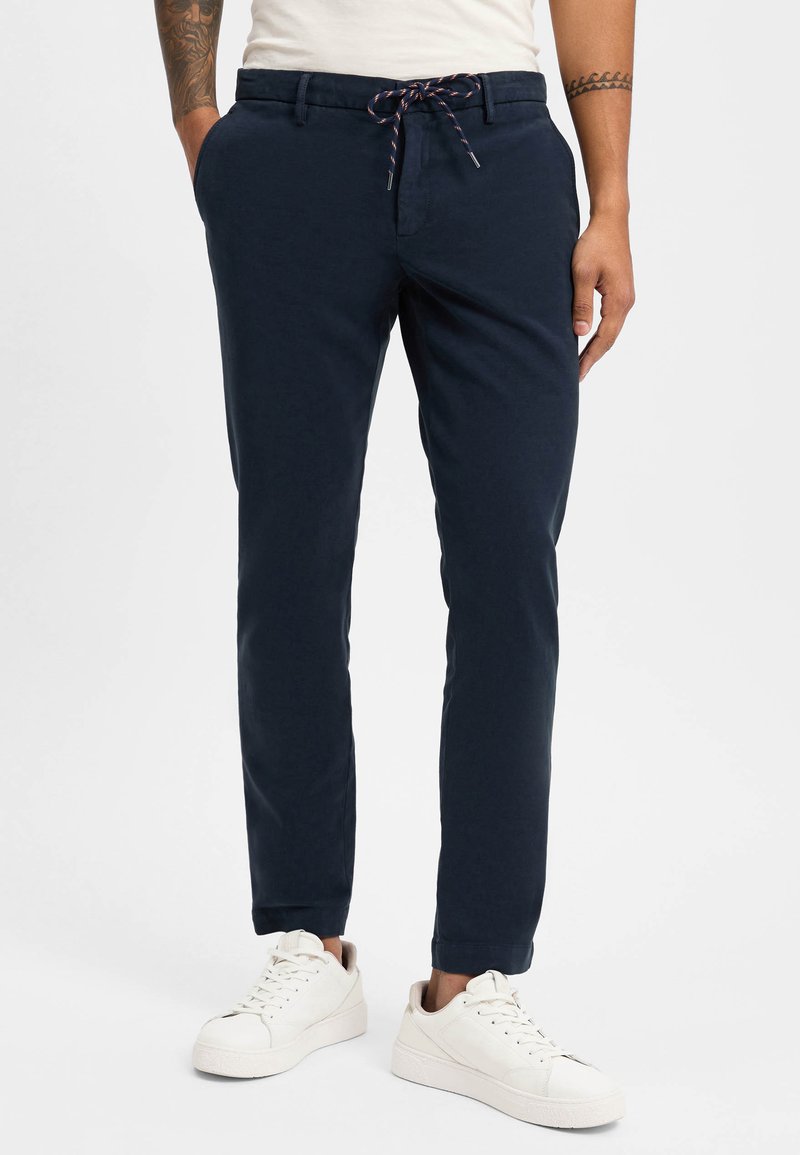 Navy blue, slim-fit pants with a drawstring waist and side pockets, made from a lightweight fabric. Worn with white sneakers.