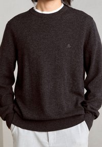 Dunkelgrauer Strickpullover mit Rundhalsausschnitt, gerippten Bündchen und Saum. Besitzt ein kleines, gesticktes Logo auf der Brust. Weicher Stoff.