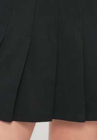 Czarna plisowana spódnica o gładkiej fakturze, z dopasowanym przeszyciem i równym dołem. Materiał wydaje się lekki i nieco elastyczny.