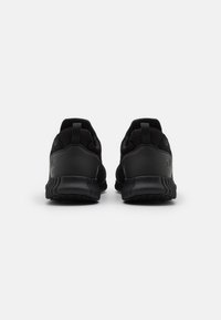 Black athletic shoes with mesh upper, padded heel, and textured sole. Features a pull tab and subtle logo detail on the heel.