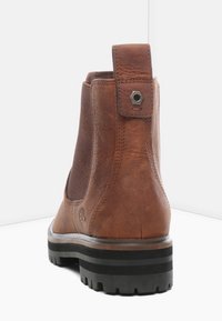 Hnědá kotníková bota z kůže s elastickými bočními panely, texturovaným povrchem, gumovou podrážkou a zdobným podpatkem; vybavena poutkem pro snadné obouvání.