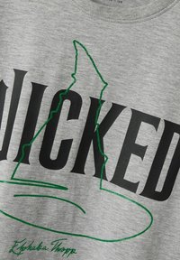 Sweatshirt gris avec "WICKED" en lettres noires en gras. Un contour pailleté vert d'un chapeau de sorcière est fièrement affiché.