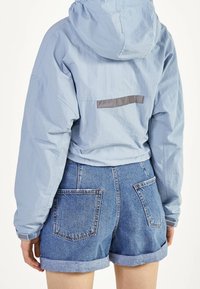 Light blue, lightweight jacket with a hood and a gray horizontal strip on the back. Paired with rolled-up denim shorts featuring patch pockets.
