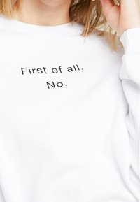 Sweatshirt blanc avec un texte noir qui dit "Premièrement, non." Tissu doux avec une coupe décontractée et des poignets côtelés.