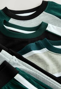 Gestapelte Baumwoll-T-Shirts in Schwarz, Grau, Grün und Teal mit gerippten Kragen und verschiedenen Farbblockdesigns. Glatte, weiche Texturen sind sichtbar.