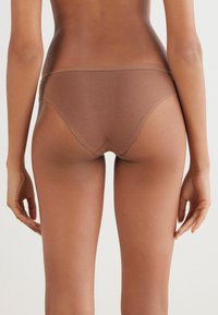 Brown seamless bikini slip met een zachte, rekbare textuur. Lage taille en minimale bedekking, met een schone elastische tailleband.
