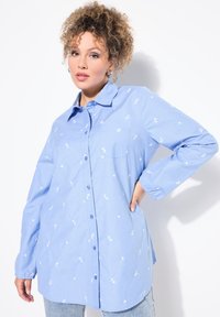 Camicia azzurro chiaro con ricami floreali bianchi, maniche lunghe con polsini abbottonati e taschino sul petto. Tessuto morbido con una vestibilità comoda.