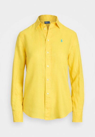 Žuta lanena košulja s gumbima, ovratnikom, dugim rukavima i svijetloplavim logotipom izvezenim na lijevoj strani prsnog dijela.
