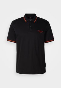 Polo noir avec des accents rouges sur le col et les manches. Il présente un col à boutons et un logo Porsche BOSS brodé en rouge.