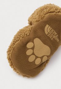 Barna gyapjú papucs talp, amelyen tappancsnyom mintázat és a The North Face logó látható, fehér háttéren.