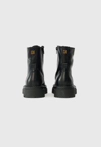 Bottes de cheville en cuir noir avec une finition texturée, un col rembourré et une semelle en caoutchouc épaisse. Présente un logo doré "SM" à l'arrière.