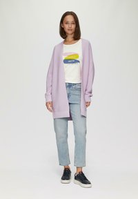 Cardigan en maille lavande avec texture côtelée sur t-shirt blanc avec un texte coloré, associé à un jean bleu et des baskets noires.