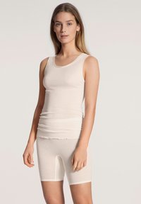Beige tanktop en shortset, gemaakt van zacht materiaal. Tanktop heeft een ronde hals en een getailleerd ontwerp; de shorts hebben een gekartelde zoom.