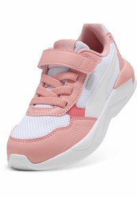 La sneaker présente un schéma de couleurs rose et blanc, des matériaux en maille et en cuir synthétique, un design à lacets avec une sangle Velcro, et une épaisse semelle blanche.