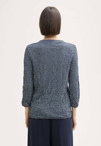 Blouse marine avec un motif texturé de petites lignes verticales, manches trois-quarts et taille cintrée, fabriquée en tissu léger.