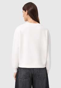 Λευκό φούτερ με στρογγυλή λαιμόκοψη και ωμούς που πέφτουν, με ριμπ μανσέτες και τελείωμα. Φορεμένο με σκούρο τζιν παντελόνι φαρδύ στο πόδι.