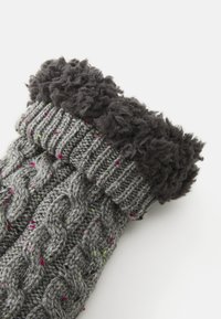 Calza grigia lavorata a maglia con un motivo a treccia, rifinita con un polsino spesso e pieno di texture di colore grigio scuro. Presenta macchie colorate nella lavorazione.