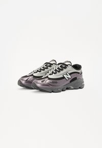Sneaker New Balance neri e viola metallico con materiali in rete e sintetici, caratterizzati da un design arrotondato e prominenti dettagli del logo.