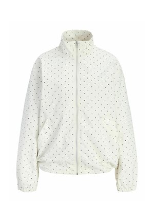 Veste blanche zippée avec des pois noirs, col montant, poignets élastiques et ourlet légèrement froncé.