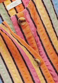 Chemise boutonnée multicolore avec des rayures verticales orange, rose, jaune et noir. Tissu texturé notable et gros boutons.