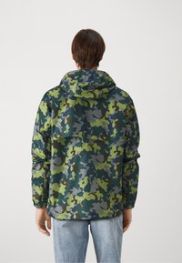 Giacca mimetica con finitura morbida e lucida. Presenta diverse tonalità di verde, blu e marrone. Comprende un cappuccio e polsini elasticizzati.