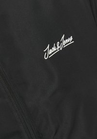 Czarna kurtka o gładkiej fakturze, z wyraźnym białym logo "Jack & Jones" oraz zapięciem na zamek po boku.