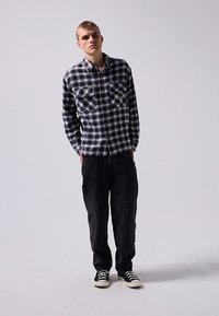 Black and white checkered flannel shirt with two front pockets, paired with dark pants and black sneakers. Texture appears soft and casual.