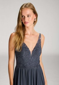 Langes dunkelgraues Kleid mit einem tiefen V-Ausschnitt und aufwendigen floralen Spitzen-Details sowie einem fließenden Rock. Glattes Gewebe mit eleganter Textur.
