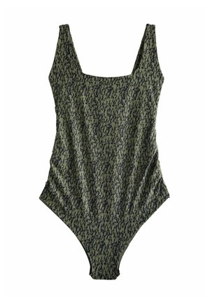 Žena s hnedými vlasmi po plecia, oblečená v sivé a čierne vzorované jednodielne plavky, stojaca chrbtom ku kamere.