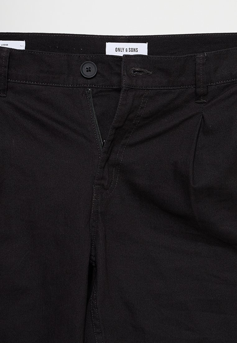 Schwarze Hose mit einem Knopf und teilweise geöffnetem Reißverschluss, mit einem weißen Etikett mit "ONLY & SONS" am Bund.
