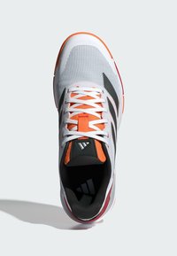 Sportieve schoen met een witte mesh bovenkant, oranje accenten en drie zwarte strepen. Heeft platte veter en een gevoerde zwarte binnenkant.