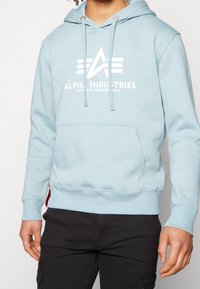 Felpa con cappuccio azzurro chiaro con logo bianco e testo, dotata di tasca frontale, coulisse e polsini a coste. Tessuto morbido, design casual.