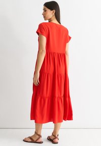 Red tiered midi dress with short sleeves, made of smooth fabric. Features gathered sections for added texture and a relaxed fit.