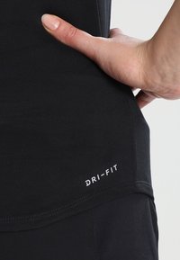Camiseta deportiva negra Dri-Fit con un diseño ajustado, textura suave y un pequeño logo blanco en el dobladillo, con una mano apoyada en la tela.