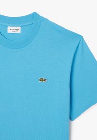 Světle modré bavlněné tričko s kulatým výstřihem a krátkými rukávy. Na levém prsu je vyšité malé zelené logo krokodýla.