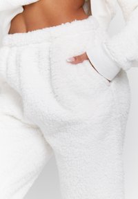 Pantalons de jogging blancs et duveteux en polaire texturée, avec une poche sur le côté et une taille élastique dotée de poignets côtelés pour un ajustement confortable.