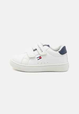 White leather sneaker with two Velcro straps, a navy heel cap, and a small logo with red and blue accents. Smooth texture, round toe.