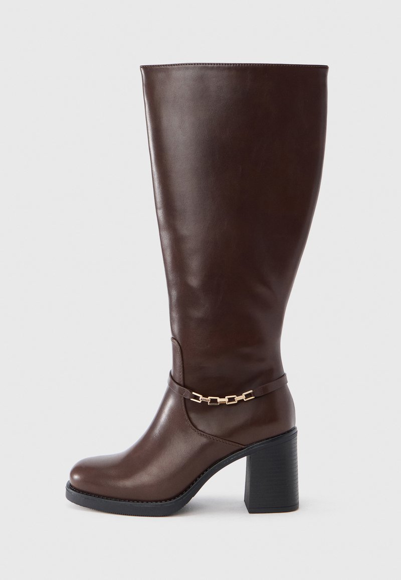 Καφέ δερμάτινη μπότες μέχρι το γόνατο με τετράγωνη μύτη, χοντρό τακούνι και χρυσή αλυσίδα γύρω από τον αστράγαλο. Λείο υλικό και κομψός σχεδιασμός.