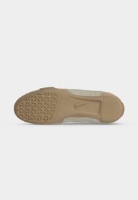 Σόλα μπεζ παπουτσιού Nike με υφή πρόσφυσης και λείο τμήμα στη φτέρνα, σε λευκό φόντο.