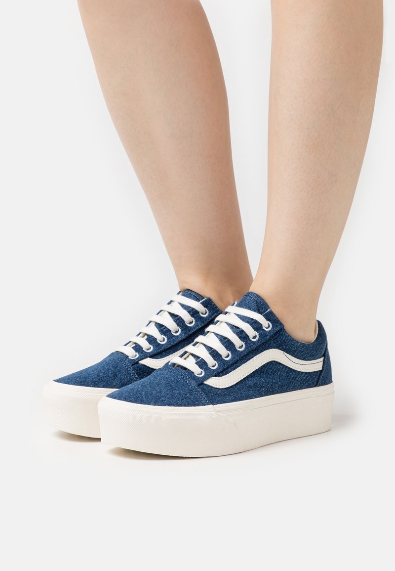 Sneakers in denim blu con suola e lacci in gomma bianca, caratterizzati da un design a swoosh bianco sul lato. Tessuto morbido, design a basso profilo.