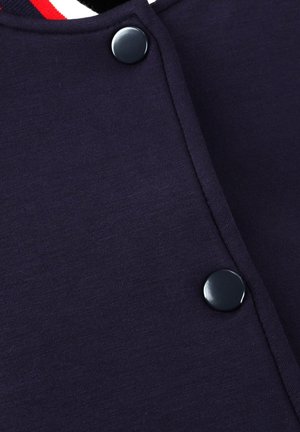 Marineblauw overhemd met knopen, met een gladde textuur, voorzien van zwarte knopen en een wit/rood gestreepte kraag. Focus op strakke lijnen en functioneel ontwerp.