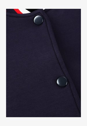 Marineblauw overhemd met knopen, met een gladde textuur, voorzien van zwarte knopen en een wit/rood gestreepte kraag. Focus op strakke lijnen en functioneel ontwerp.