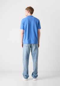 Hellblaues Polohemd aus Baumwolle, mit kurzen Ärmeln und lockerer Passform, kombiniert mit hellblauen Jeans und weißen Turnschuhen.