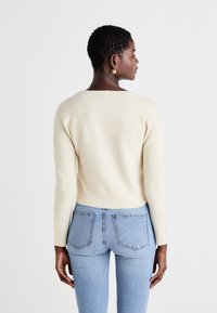 Kremfarget genser i mykt, fluffy materiale, med rund hals og lange ermer, paret med lyseblå, tettsittende jeans.