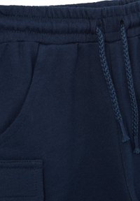 Pantalones de chándal azul marino con un tejido texturizado, que cuentan con una cintura elástica, cordón y un bolsillo lateral. Diseño moderno y sencillo.